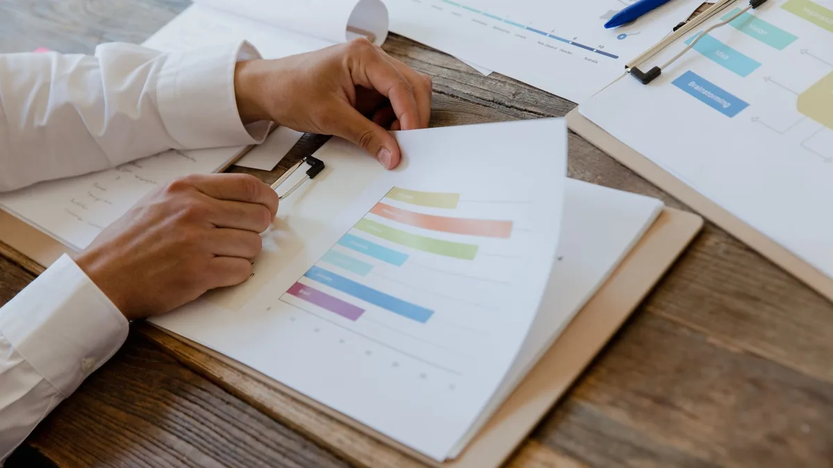 Close-up of hands reviewing business report with colorful charts and graphs on a wooden desk.