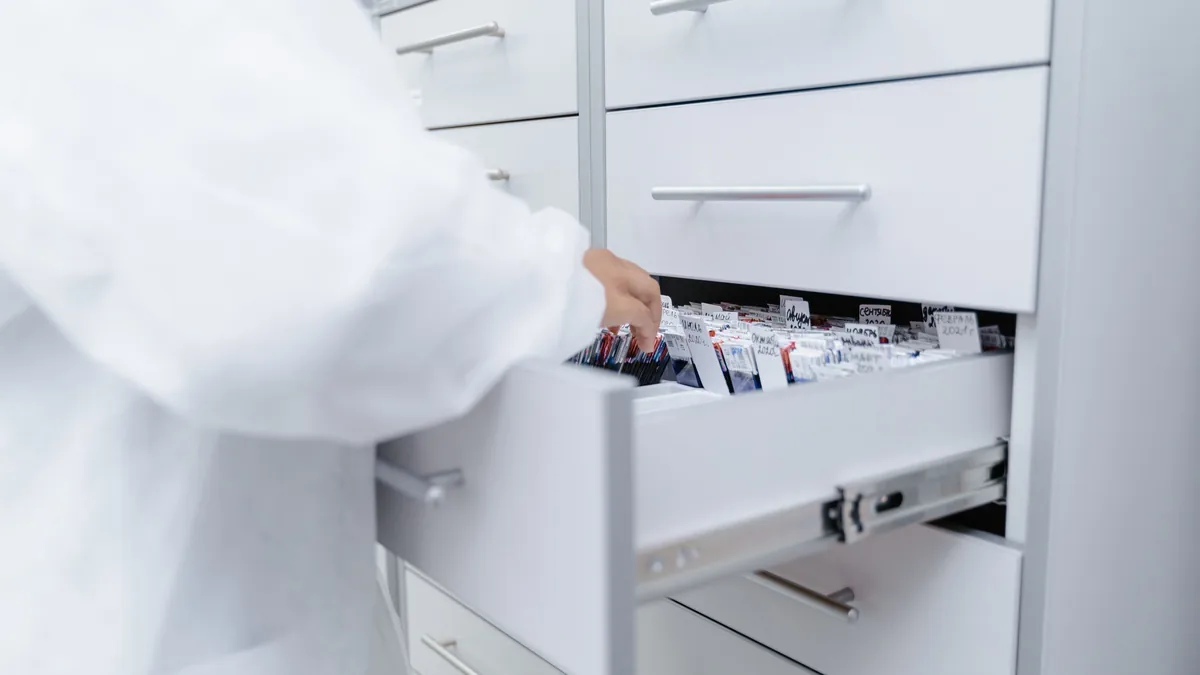 A hand pulls open a drawer of stored medication, the controlled supply that drug diversion reviews track